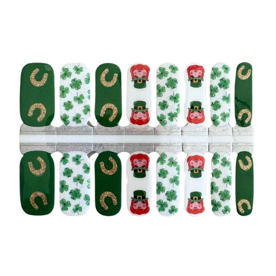 A close-up photo of St. Patrick’s Day Nail Wraps featuring a vibrant white base adorned with shamrocks, horseshoes, and leprechauns, perfect for adding a festive touch to your manicure.