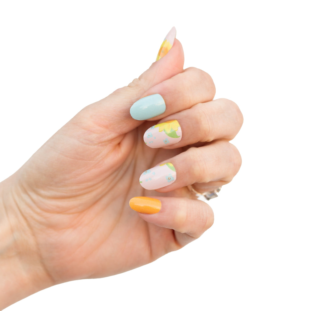 Simple Sunflower Nail Wraps - a charming and whimsical set of nail wraps featuring sunflower graphics on a soft pink, yellow, and green base, showcased on a model's hand.
