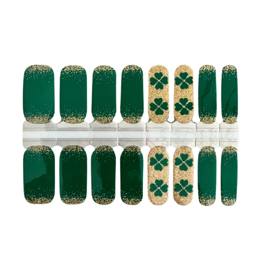 A close-up photo of St. Patrick’s Day Nail Wraps featuring a stunning green base with a captivating gold glitter ombre effect, accentuated by accent nails with a striking gold glitter base adorned with charming green shamrocks, perfect for adding a touch of Irish elegance to your manicure