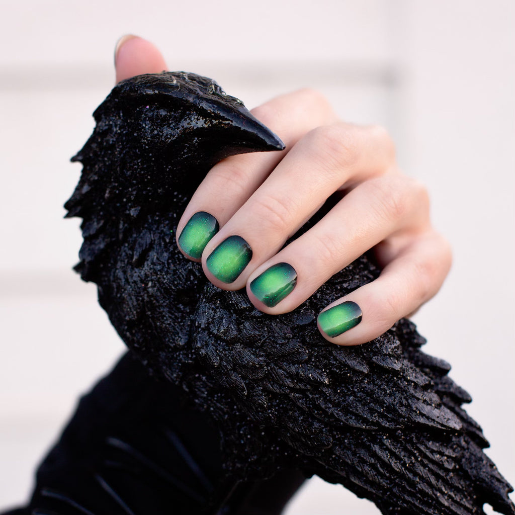 Model's hand elegantly displaying Mystic Aura gel nail stickers, highlighting the black edges and vibrant green center for a stunning aura effect.