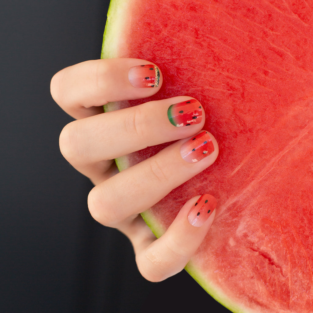 Watermelon Nail Wraps on a hand model, holding a slice of juicy watermelon - a playful and vibrant set of nail wraps featuring bold watermelon graphics on a bright red background with accents of green, complemented by a slice of fresh watermelon in hand.