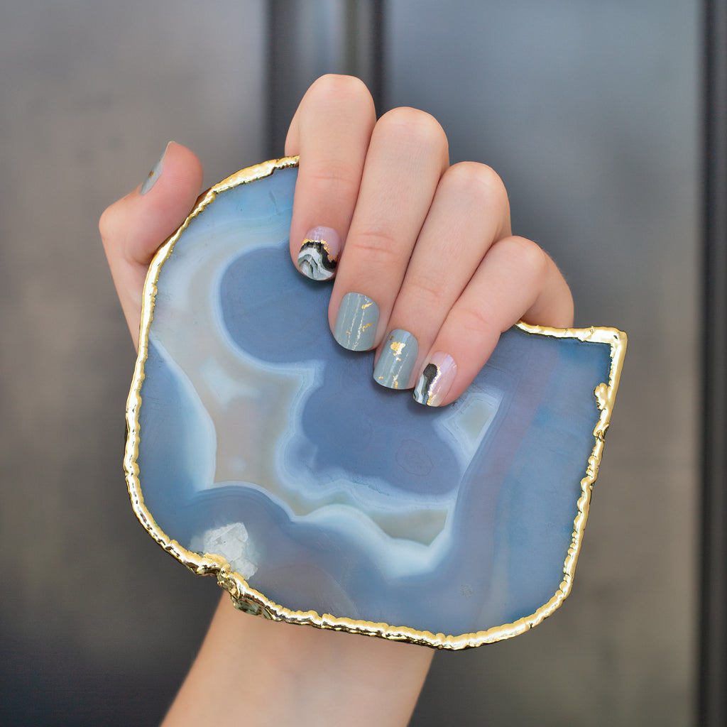Model's hand showcasing Crystal Clear nail wraps, featuring elegant black and gray geode graphics with gold foil accents on clear and gray bases, highlighting the exclusive and sophisticated design.