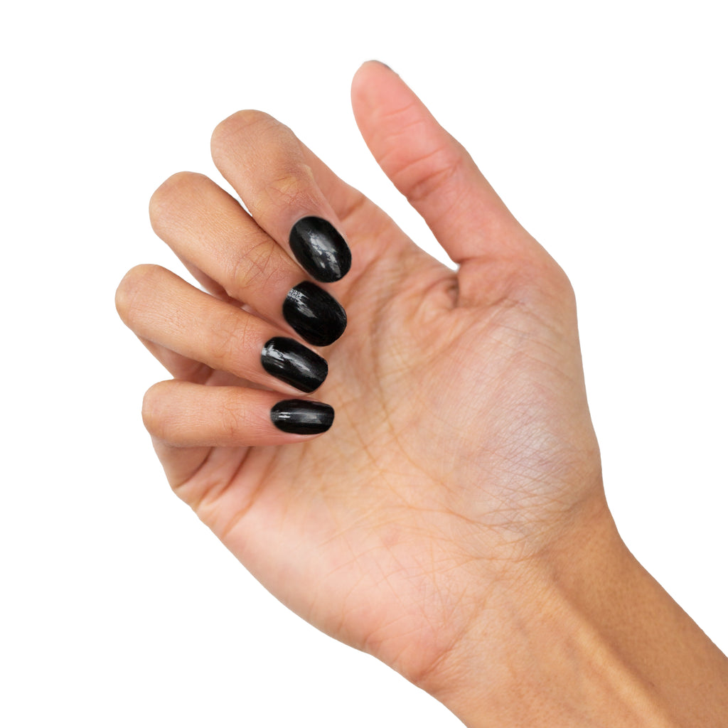 A sophisticated image of a model's hand adorned with the plain Black nail wrap by Nails Mailed. The black nail wraps showcase a seamless and professional finish, reflecting the ease and elegance of DIY gel nails at home. - NailsMailed