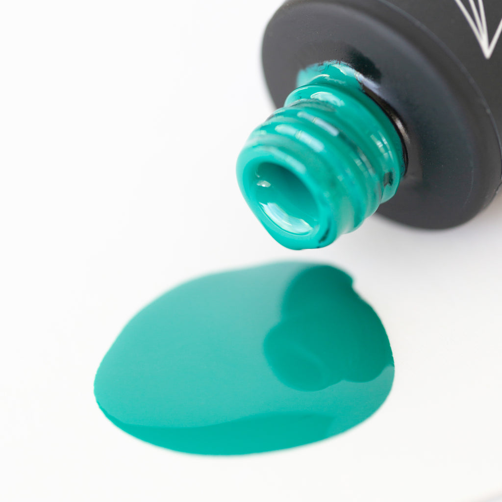 Aquamarine gel nail polish, a rich teal shade, is pictured against a white background. The round bottle has a black cap with a brush applicator sticking out of it. The light reflects off the glossy surface of the polish, highlighting the cool and refreshing teal color.