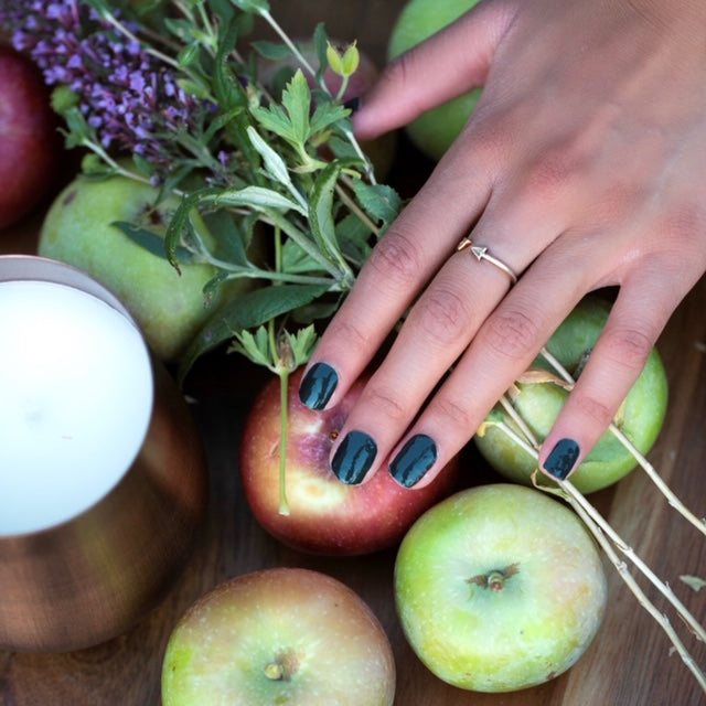 Model's hand adorned with Juniper nail wraps by Nails Mailed, placed amidst fall-themed surroundings, emphasizing the deep emerald green color that complements the autumn ambiance.