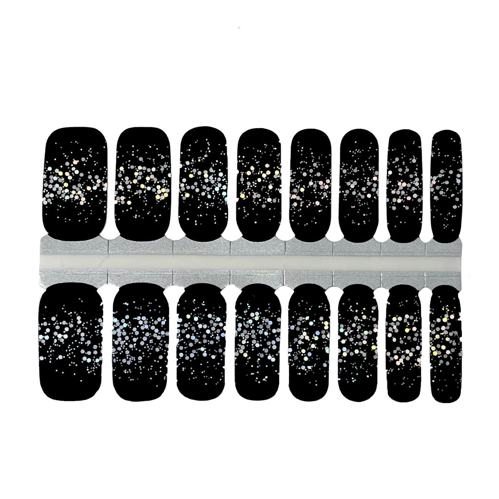 A photo of the Glitter Up nail wraps against a white background. The rectangular wraps are aligned next to each other, and their edges are slightly curved to fit the shape of a fingernail. The base of the wraps is a deep black color, while the tips feature a shimmering silver glitter. The photo is well-lit and provides a clear view of the product.