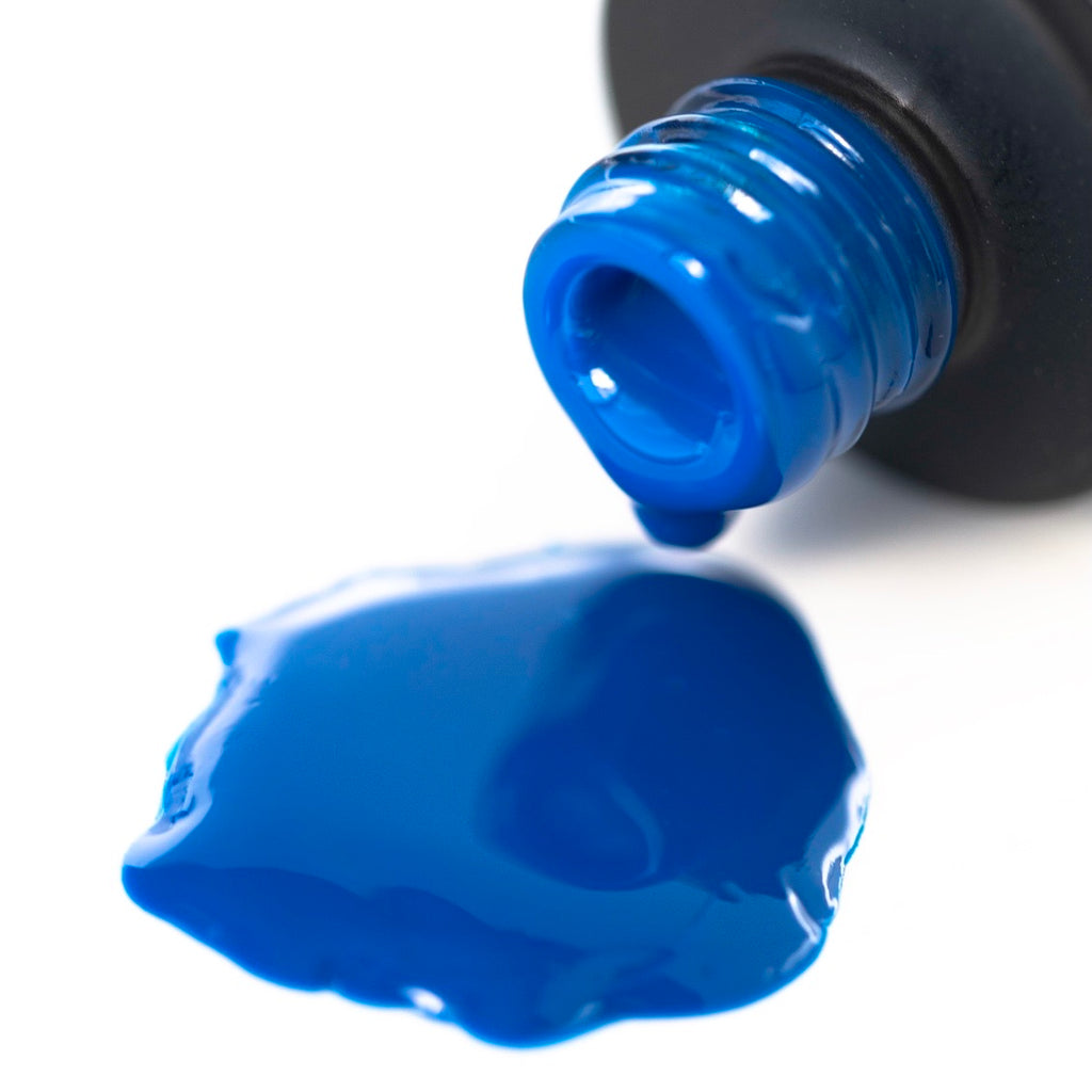 Brilliant Blue gel nail polish is shown on a white background. The round bottle has a black cap with a brush applicator sticking out of it. The bright blue polish is glossy and vibrant, making a bold statement.